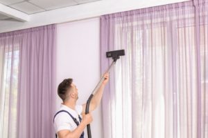 Man using vacuum to clean window treatments in Dallas